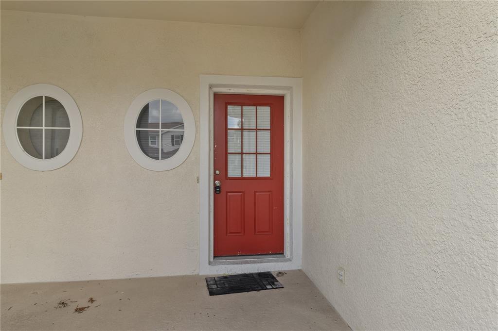 A red door with a window sits on a porch next to two circular windows — 1147 JONAH DRIVE, NORTH PORT, FL