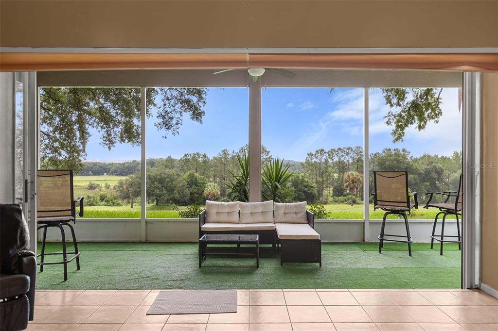 A screened-in patio with artificial turf, outdoor furniture, and a view of a grassy field — 2390 CALEDONIAN STREET, CLERMONT, FL