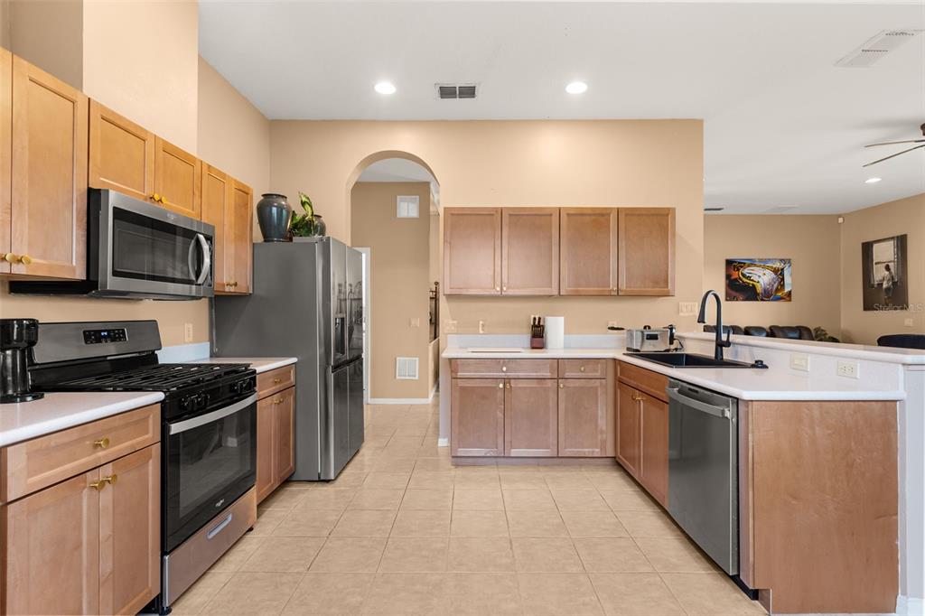 A kitchen features light wood cabinets, stainless steel appliances, and beige tile flooring — 2390 CALEDONIAN STREET, CLERMONT, FL