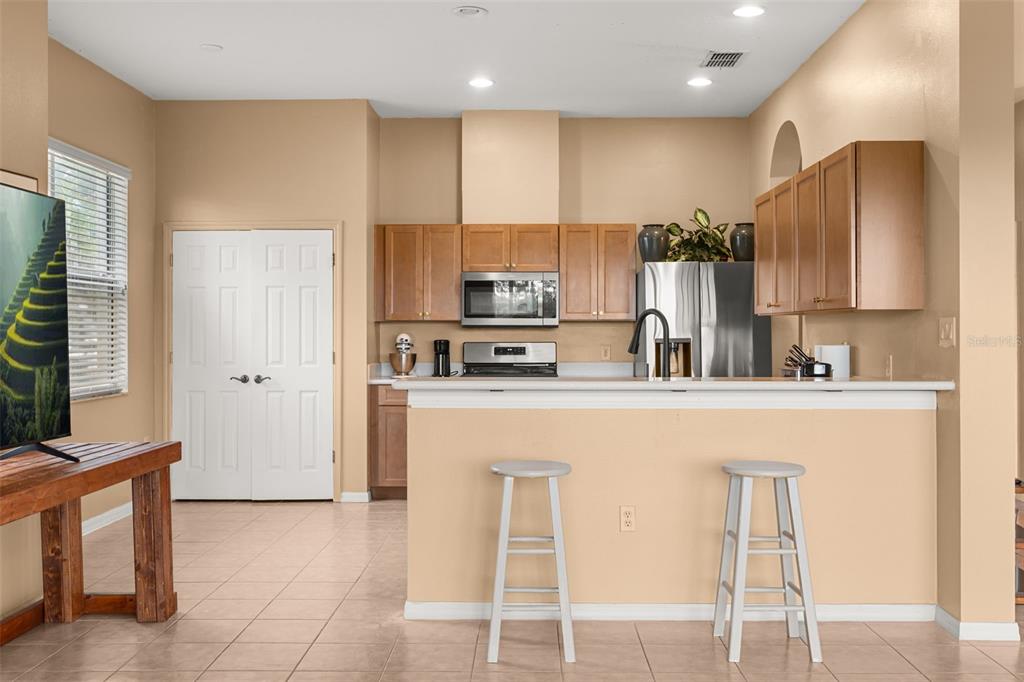A kitchen features light wood cabinets, stainless steel appliances, a breakfast bar with stools, and tile flooring — 2390 CALEDONIAN STREET, CLERMONT, FL