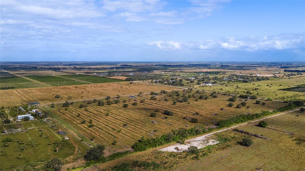 An aerial view shows a large, flat, grassy field with scattered trees and distant rural buildings — 2321 SNEED ROAD, FORT PIERCE, FL