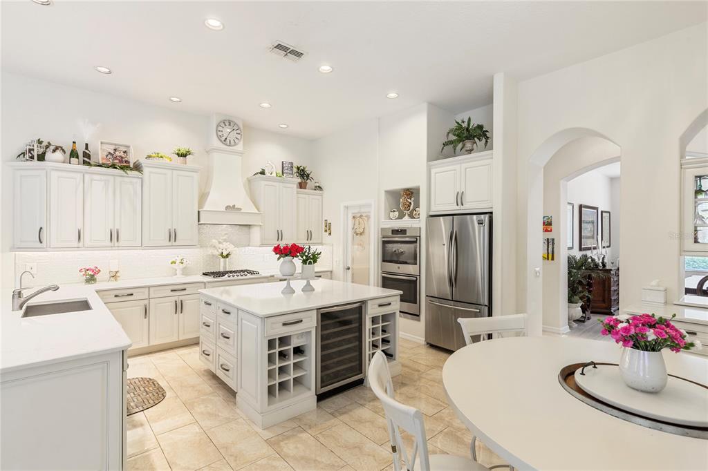 A bright kitchen features white cabinetry, a central island with a wine cooler, and tile flooring — 5603 EAGLEGLEN PLACE, LITHIA, FL