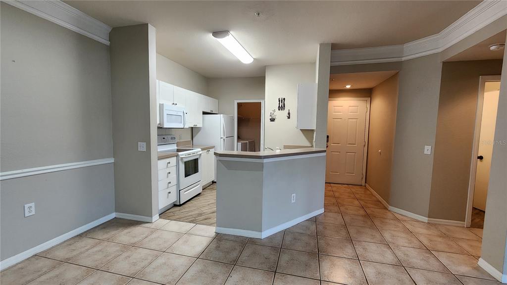 A kitchen with white cabinets, stainless steel appliances, and tile flooring opens to a hallway — 5134 NORTHRIDGE ROAD UNIT 203, SARASOTA, FL