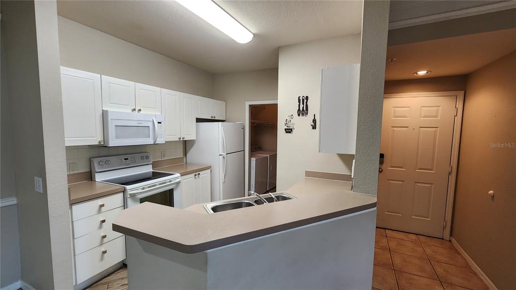 A kitchen features white cabinets, tan countertops, a white appliance suite, and a breakfast bar — 5134 NORTHRIDGE ROAD UNIT 203, SARASOTA, FL