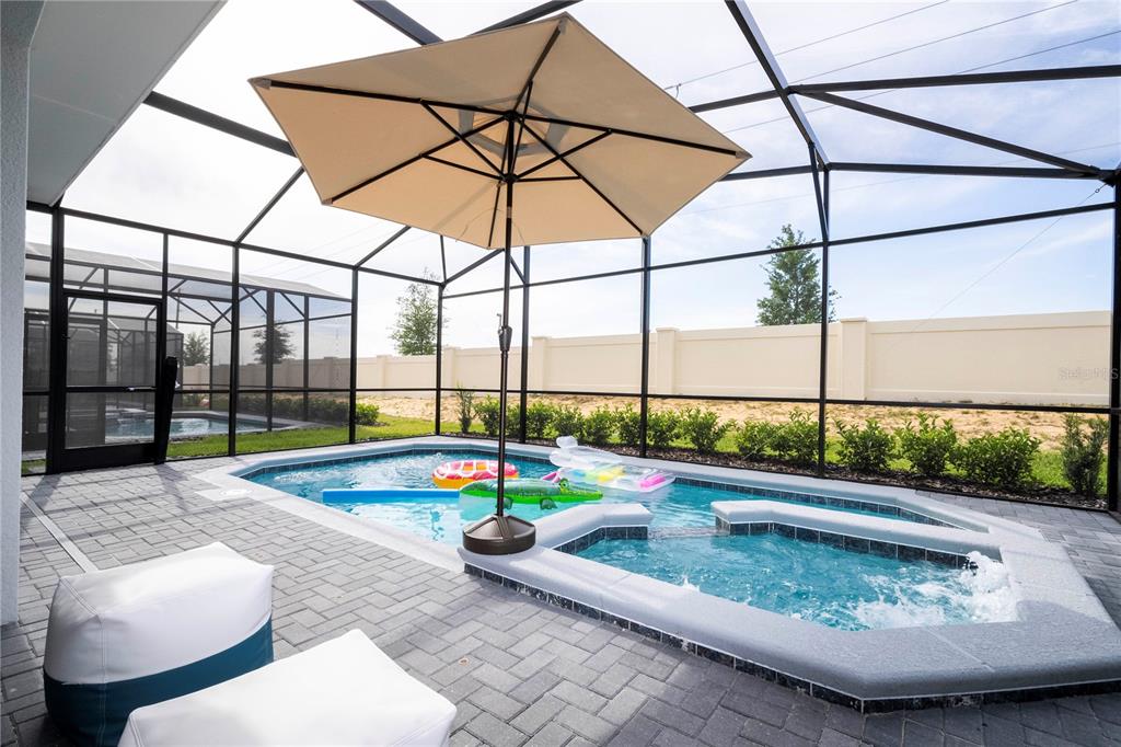 A screened-in patio features a swimming pool, a hot tub, and a large beige umbrella — 3325 LILAC WAY, DAVENPORT, FL