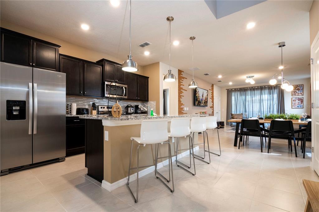 A kitchen with dark cabinets, stainless steel appliances, and a breakfast bar with white stools — 3325 LILAC WAY, DAVENPORT, FL