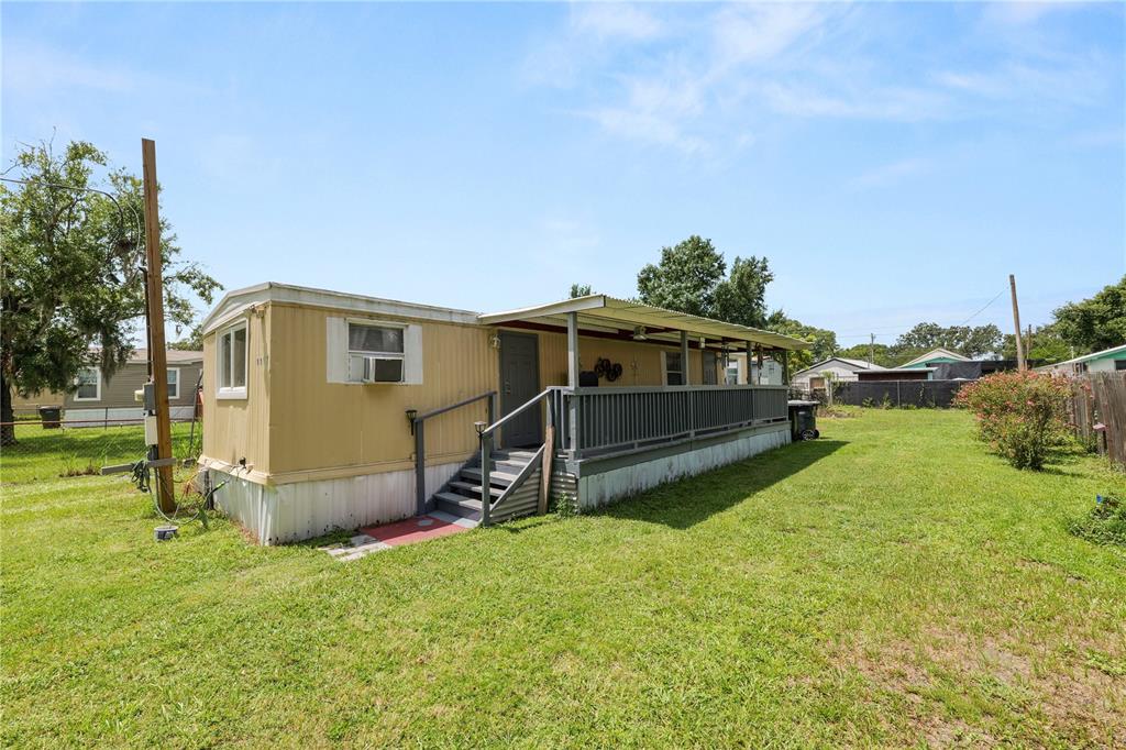 A tan mobile home features a long, covered wooden porch and stairs in a grassy yard — 1111 S TERRY AVENUE, LAKELAND, FL