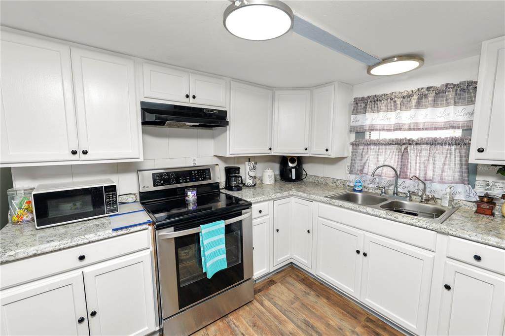 A kitchen with white cabinets, stainless steel appliances, granite countertops, and wood-look flooring — 1111 S TERRY AVENUE, LAKELAND, FL