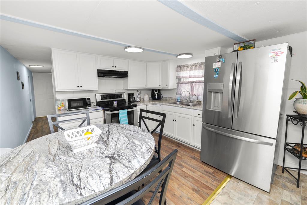 A kitchen features white cabinets, stainless steel appliances, a marble-topped table, and wood-look flooring — 1111 S TERRY AVENUE, LAKELAND, FL
