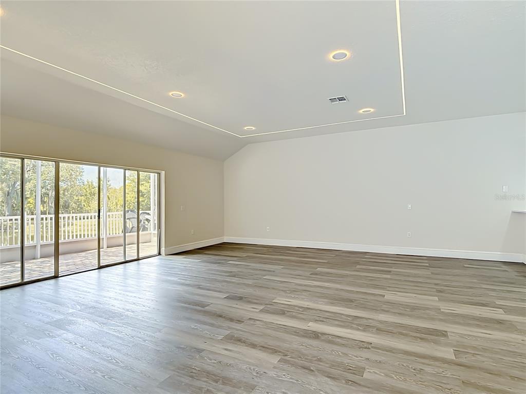 A spacious, empty room features light wood-look flooring, recessed lighting, and sliding glass doors — 1008 UNIVERSAL REST PLACE, KISSIMMEE, FL