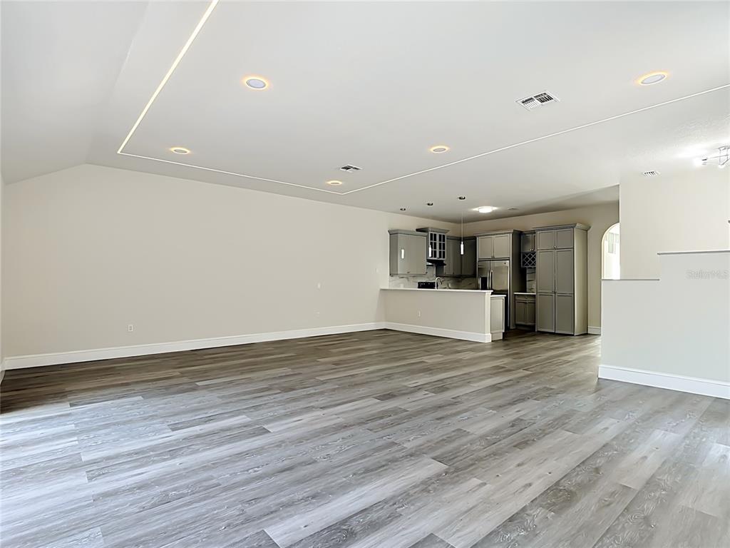 An open-concept living area features light-colored walls, recessed ceiling lighting, and grey wood-look flooring — 1008 UNIVERSAL REST PLACE, KISSIMMEE, FL