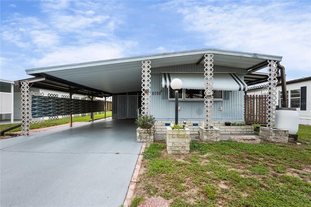 A single-story manufactured home with a large carport, lattice supports, and a stone-accented front porch — 5318 ASTRID DRIVE, ZEPHYRHILLS, FL