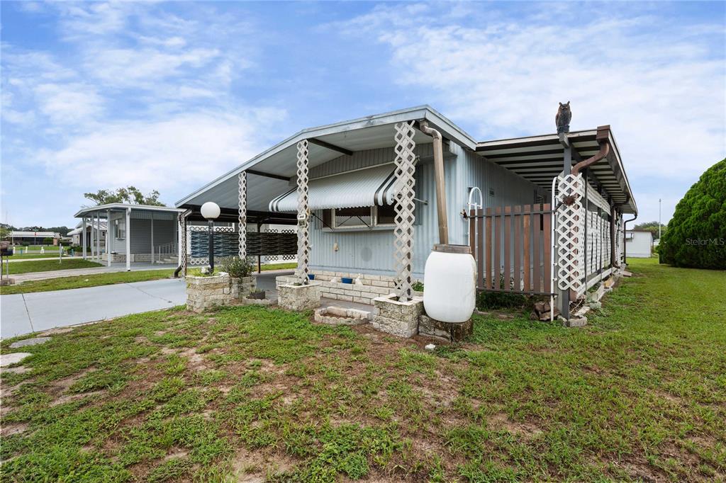 A light blue mobile home features a carport, lattice supports, and a rain barrel — 5318 ASTRID DRIVE, ZEPHYRHILLS, FL