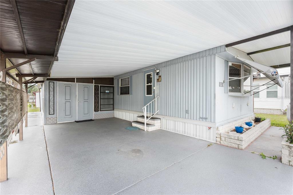 A mobile home exterior features a covered carport, a small set of stairs, and siding — 5318 ASTRID DRIVE, ZEPHYRHILLS, FL