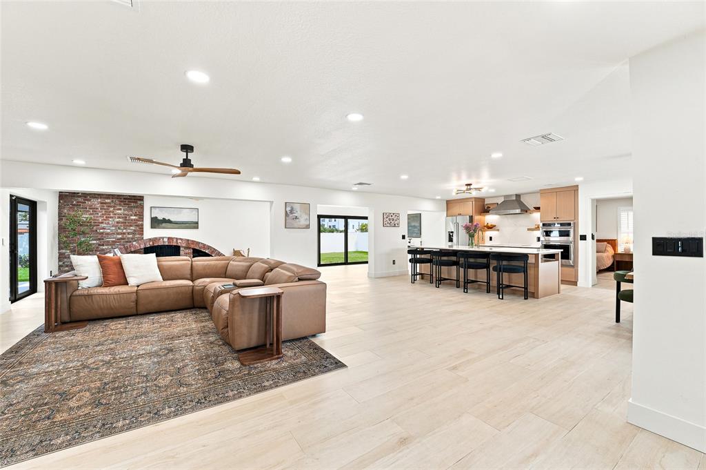 A spacious open-concept living room features a large leather sectional, wood flooring, and a kitchen — 6241 TANGLEWOOD DRIVE NE, ST PETERSBURG, FL