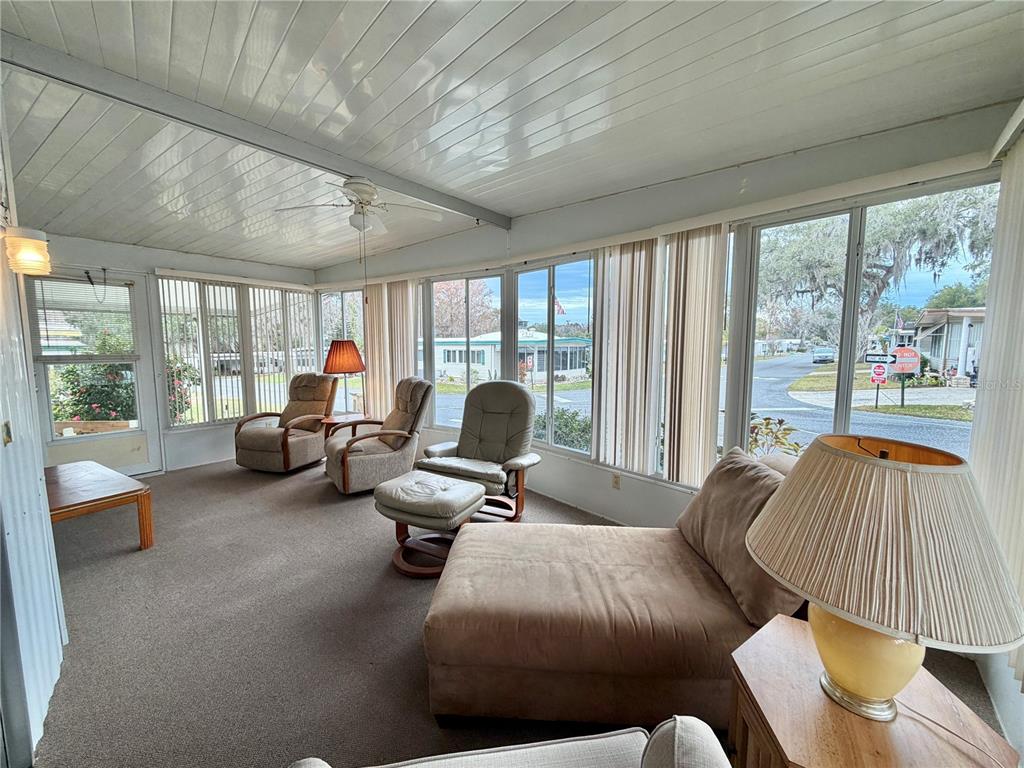 A sunroom with a carpeted floor, white paneled ceiling, and large windows overlooking a street — 211 ASPEN CIRCLE, LEESBURG, FL