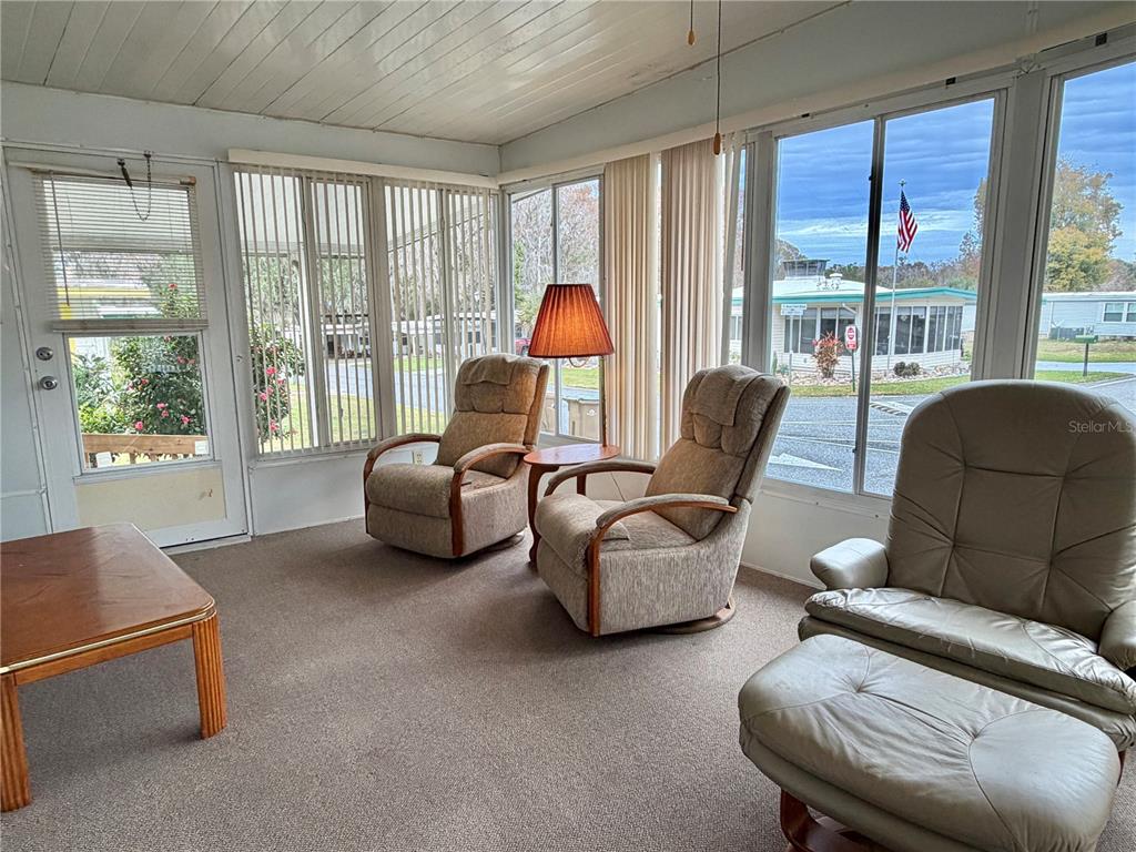 A sunroom features carpeted floors, large windows with vertical blinds, and three comfortable armchairs — 211 ASPEN CIRCLE, LEESBURG, FL