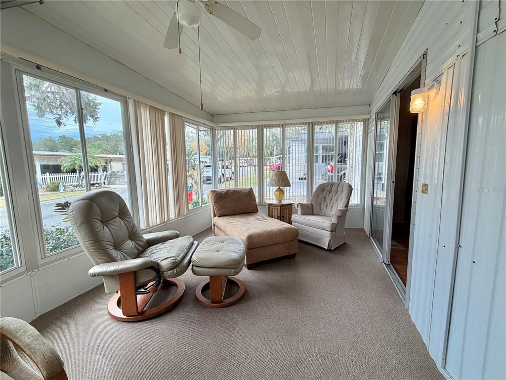 A sunroom features a ceiling fan, carpeted flooring, and multiple windows overlooking a residential street — 211 ASPEN CIRCLE, LEESBURG, FL