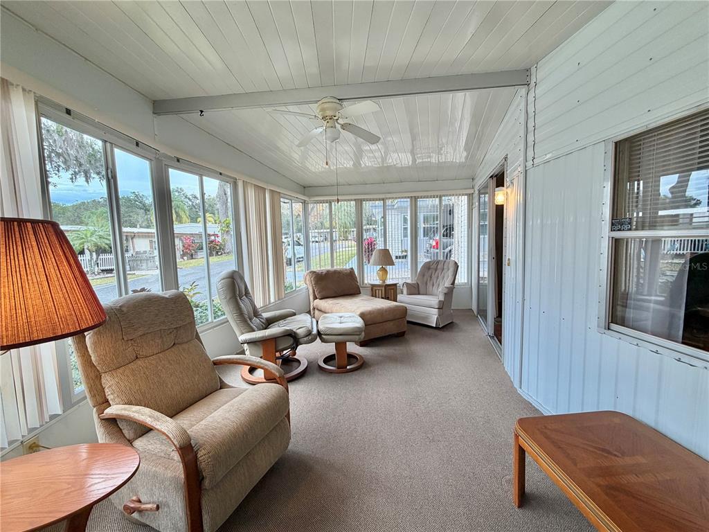 A sunroom features carpeted floors, a ceiling fan, and multiple windows overlooking a residential street — 211 ASPEN CIRCLE, LEESBURG, FL