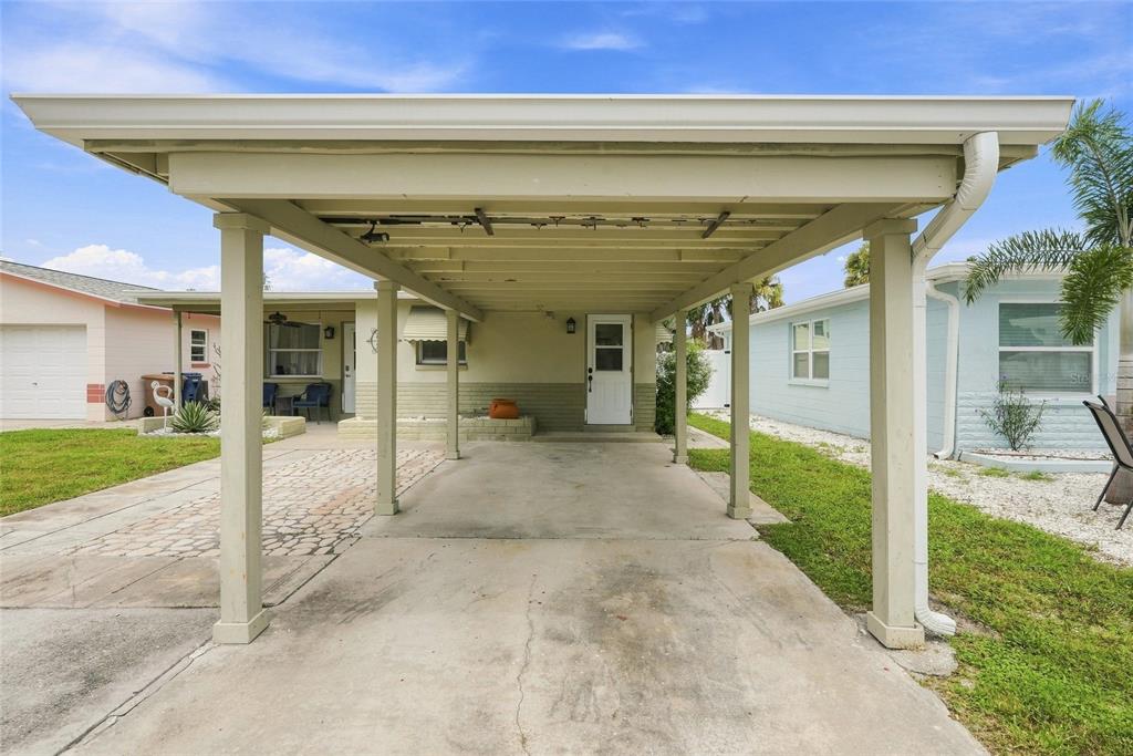 A concrete driveway leads to a covered carport attached to a single-story residential home — 13313 2ND STREET E, MADEIRA BEACH, FL