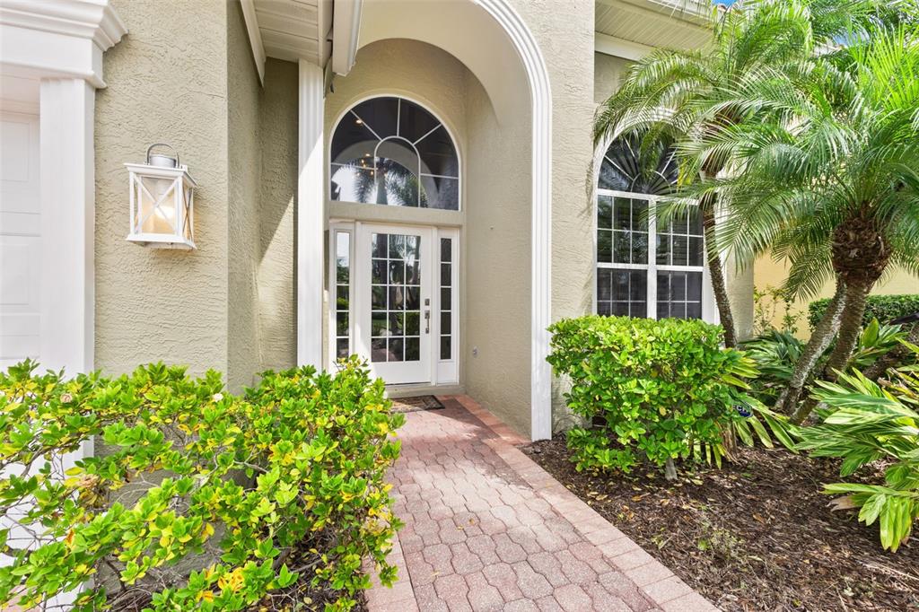 A brick walkway leads to the arched front entrance of a house with beige stucco — 304 9TH AVENUE E, PALMETTO, FL