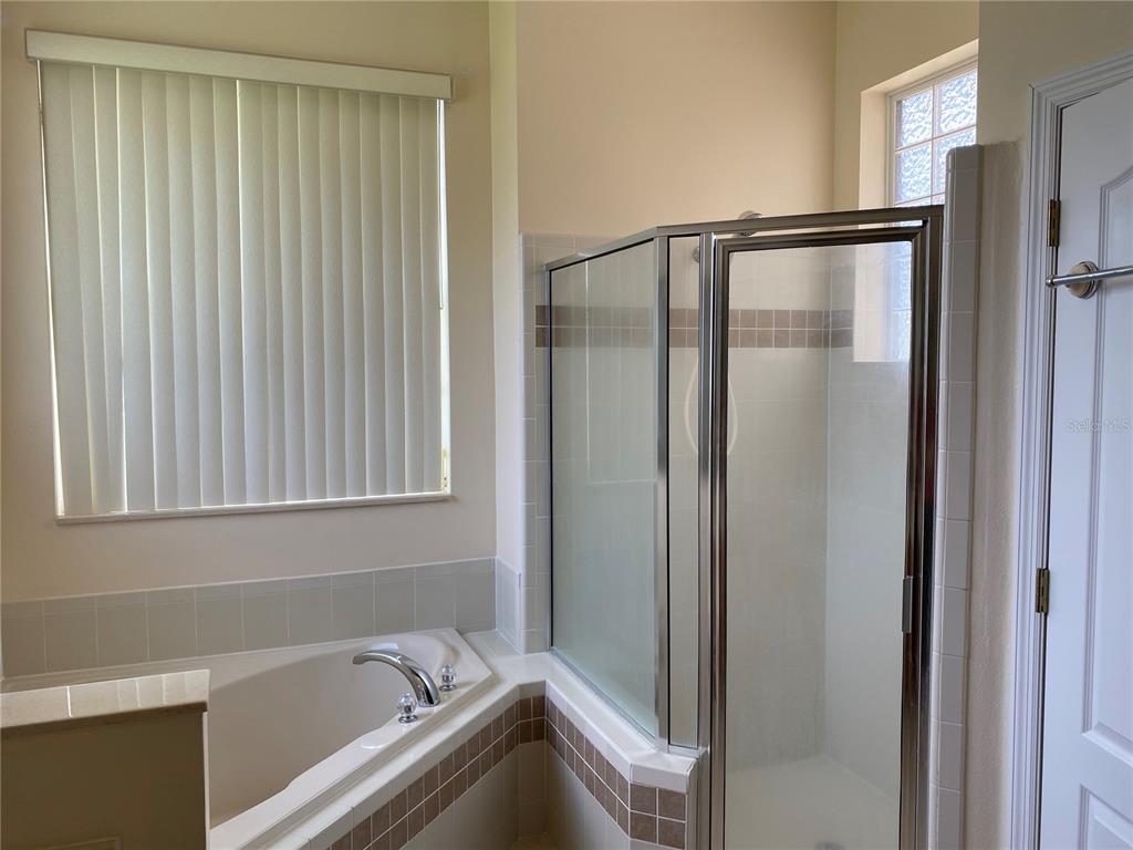 A bathroom features a corner soaking tub and a glass-enclosed shower with tiled accents — 12934 COLONNADE CIRCLE, CLERMONT, FL