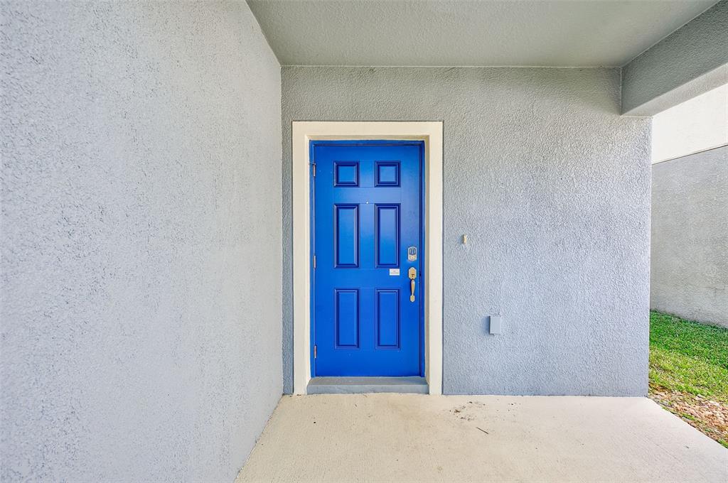 A bright blue front door with six rectangular panels sits in a gray stucco entryway — 1902 HAWKS VIEW DRIVE, RUSKIN, FL
