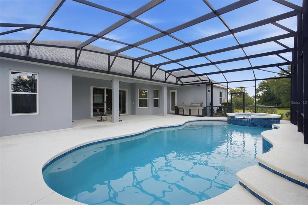 A swimming pool and spa are enclosed within a screened lanai behind a gray house — 5489 NANTAHALA LANE, LADY LAKE, FL