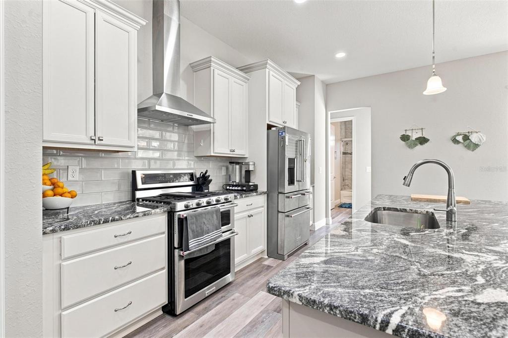 A modern kitchen features white cabinetry, granite countertops, stainless steel appliances, and a center island — 5489 NANTAHALA LANE, LADY LAKE, FL