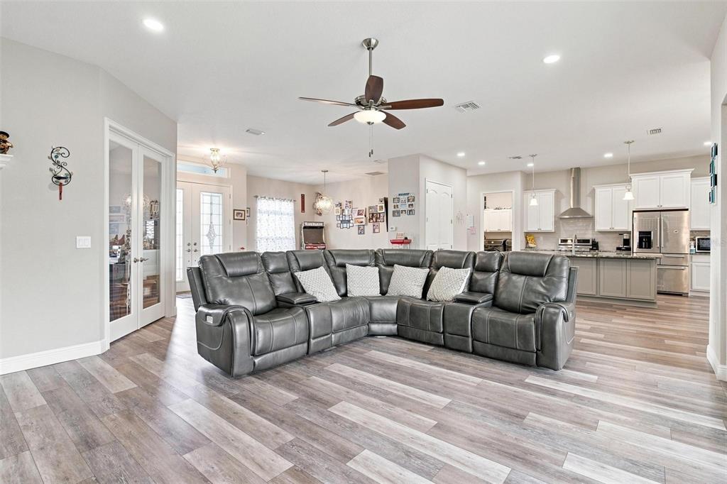 An open-concept living room features a large gray sectional sofa and wood-look flooring — 5489 NANTAHALA LANE, LADY LAKE, FL