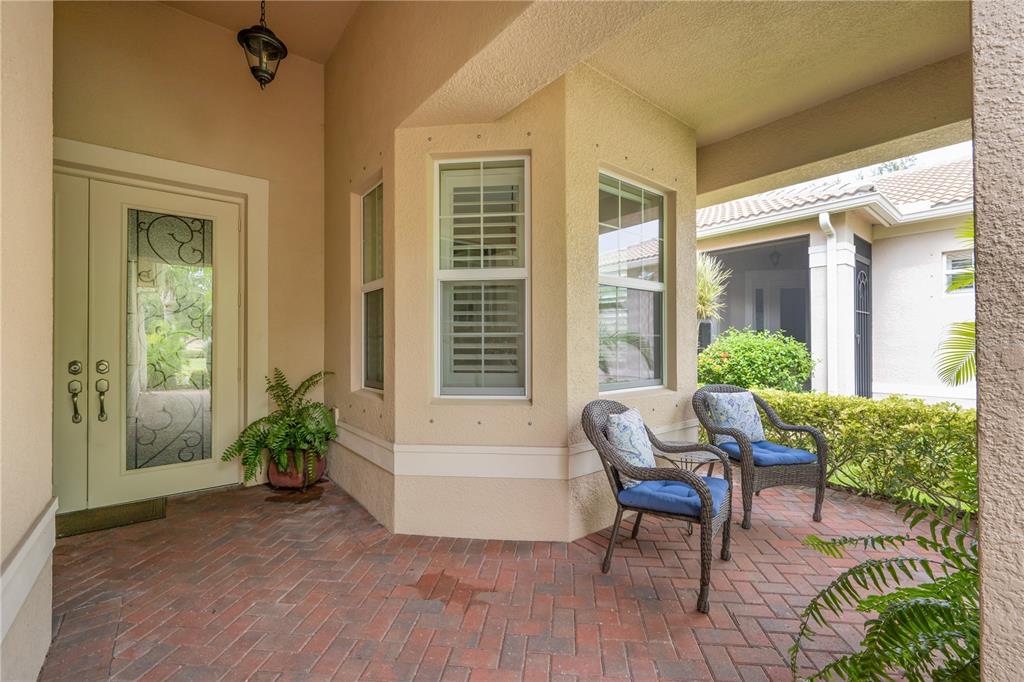 A covered brick patio features two wicker chairs, a glass-paneled door, and large windows — 4952 SANDY GLEN WAY, WIMAUMA, FL