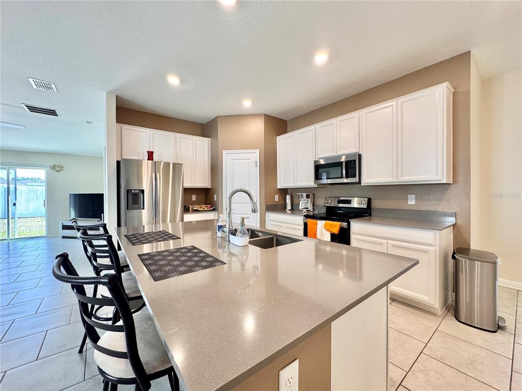 A kitchen features white cabinets, stainless steel appliances, a large island, and light-colored tile flooring — 913 WASHINGTON STREET, BARTOW, FL
