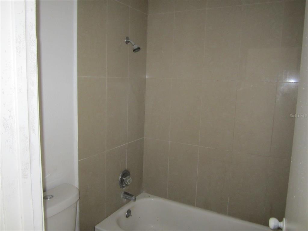A bathroom features a white bathtub with a showerhead and tan tiled walls — 4011 E COLUMBUS DRIVE, TAMPA, FL