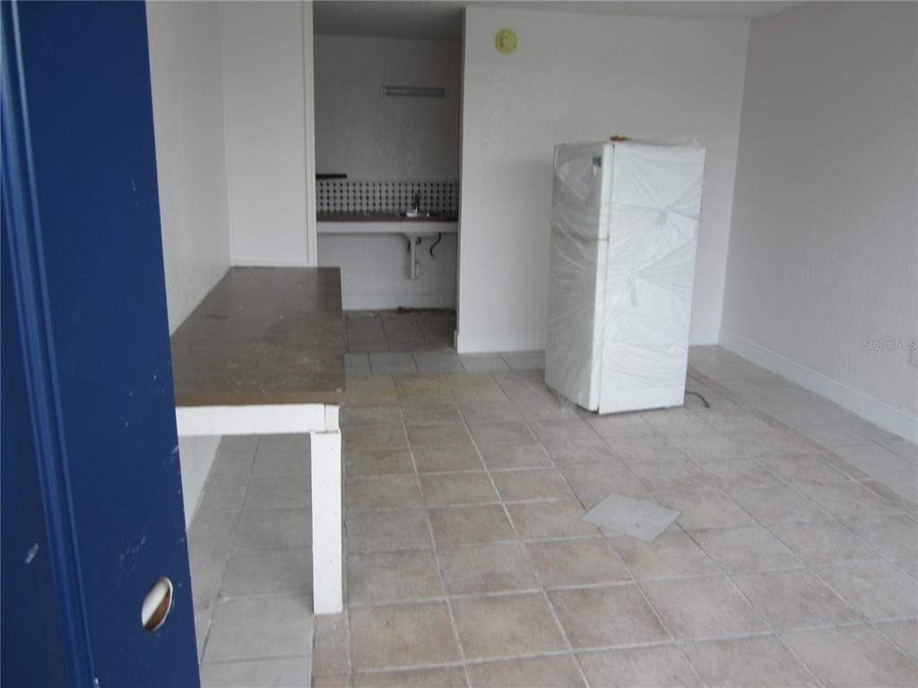 An unfurnished room features tiled floors, a table, and a refrigerator wrapped in plastic — 4011 E COLUMBUS DRIVE, TAMPA, FL