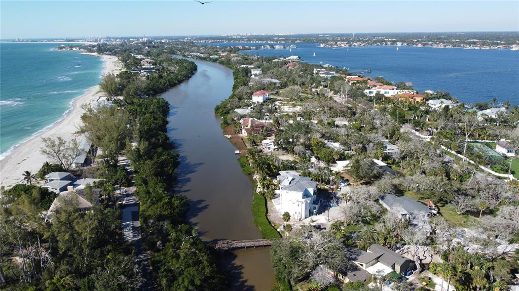An aerial view shows a narrow waterway separating a beach from a residential neighborhood — 8534 HERON LAGOON CIRCLE, SARASOTA, FL