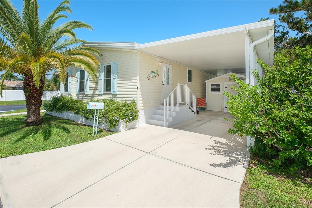 A light-yellow mobile home features a palm tree, a concrete driveway, and a covered carport — 1800 ENGLEWOOD ROAD UNIT 26, ENGLEWOOD, FL