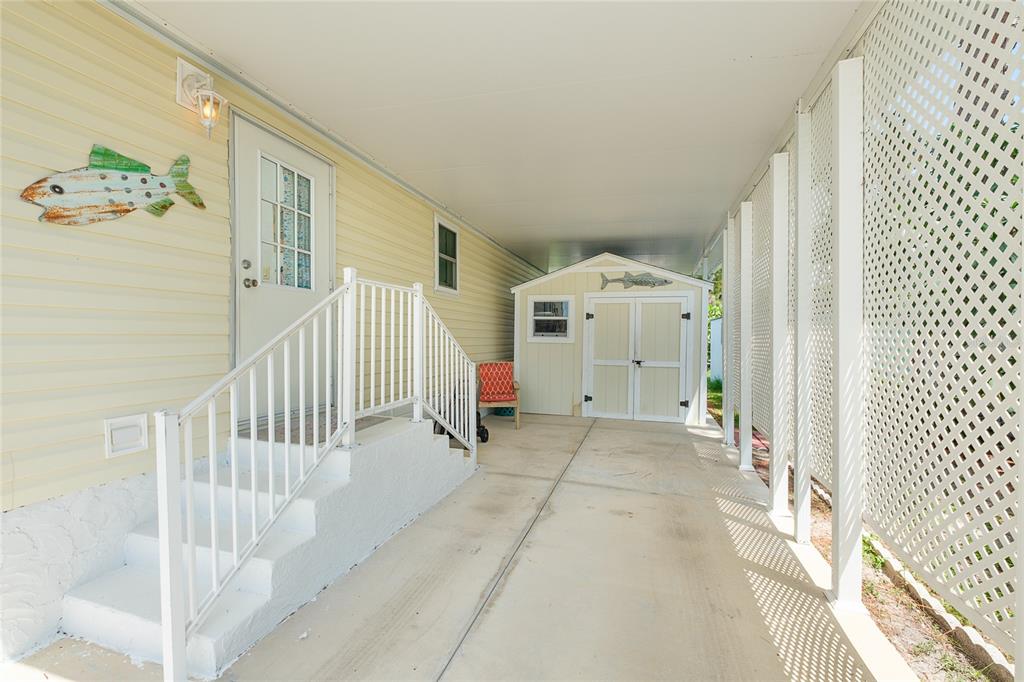A covered carport features a concrete floor, a storage shed, and stairs leading to a door — 1800 ENGLEWOOD ROAD UNIT 26, ENGLEWOOD, FL