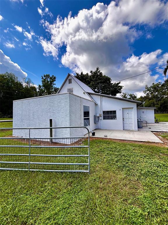 A white stucco house with a metal roof and a concrete patio sits in a yard — 9499 TREIMAN BOULEVARD, WEBSTER, FL