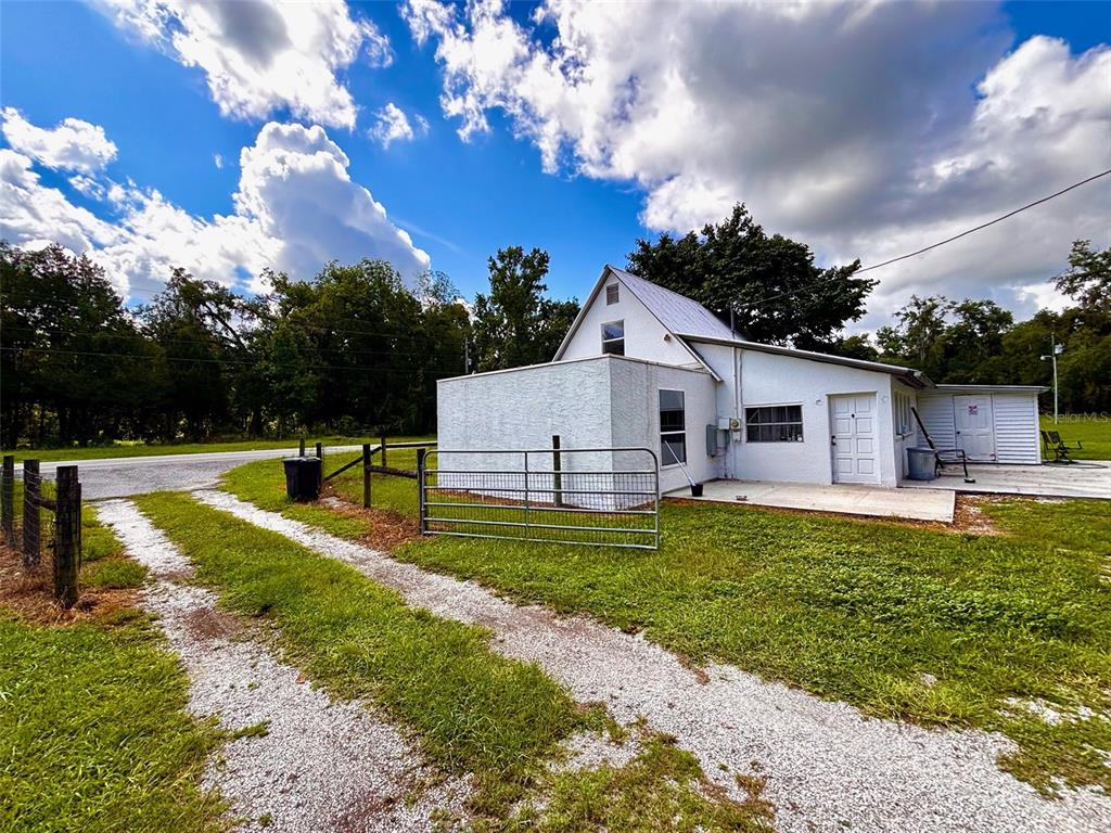 A white house with a metal roof sits beside a gravel driveway and metal gate — 9499 TREIMAN BOULEVARD, WEBSTER, FL