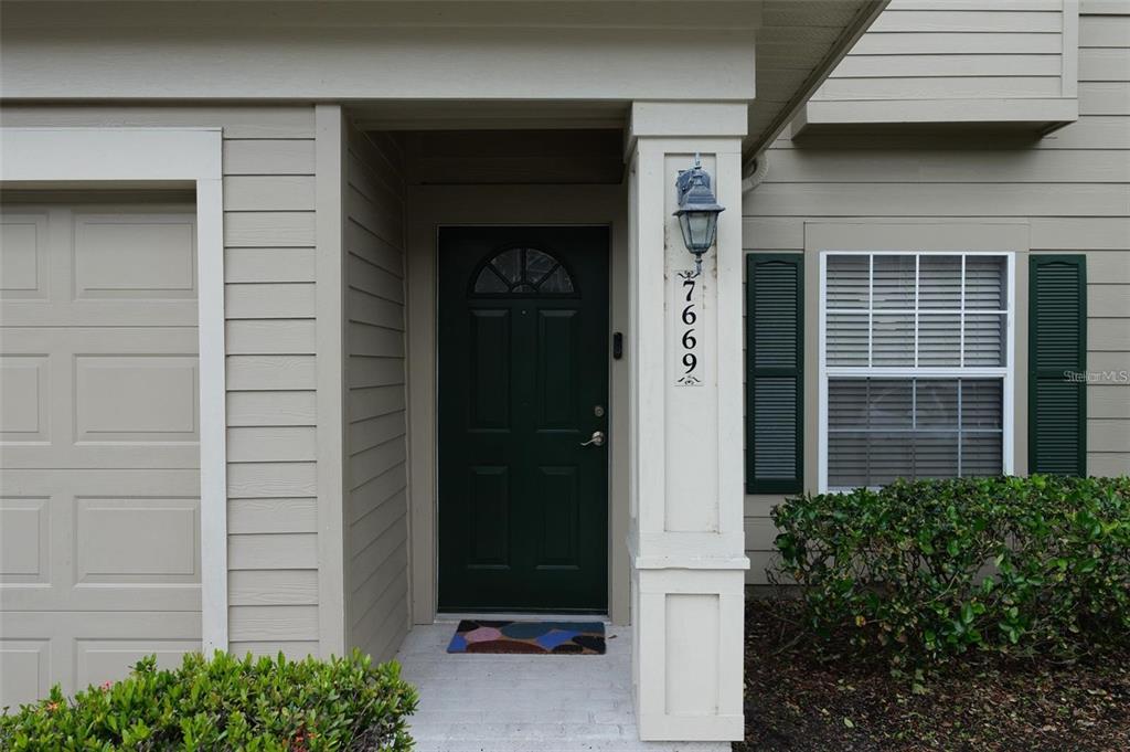 The exterior of a house features a dark green front door, a garage, and a window — 7669 PLANTATION CIRCLE, UNIVERSITY PARK, FL