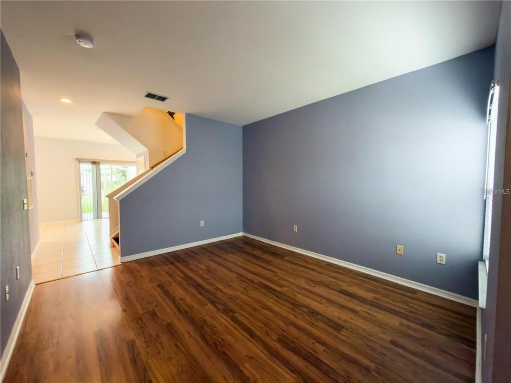An empty living room features wood-look flooring, blue walls, and a staircase leading upstairs — 7669 PLANTATION CIRCLE, UNIVERSITY PARK, FL