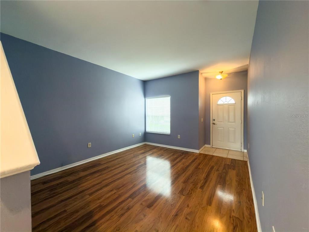 An empty room with blue walls, wood-look flooring, a window, and a front door — 7669 PLANTATION CIRCLE, UNIVERSITY PARK, FL