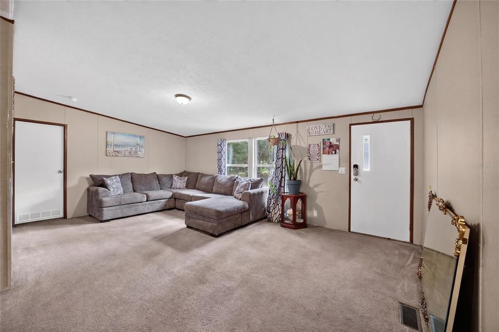 A living room features beige walls, wall-to-wall carpeting, a large sectional sofa, and an entryway — 4842 W NESTER COURT, HOMOSASSA, FL
