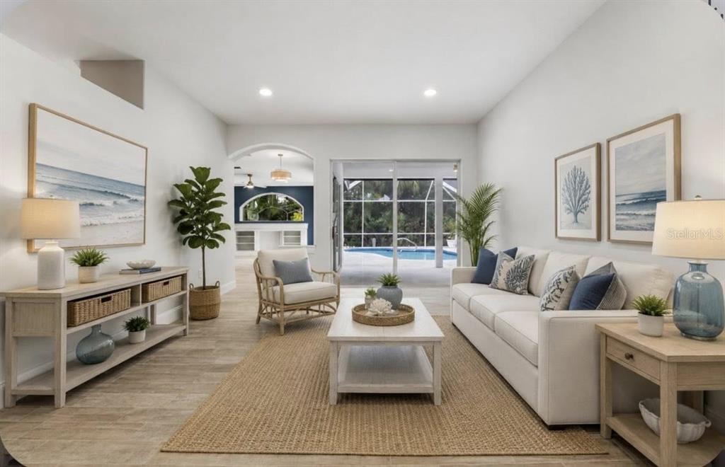 A bright living room features a white sofa, coffee table, and sliding doors to a pool — 507 CHEVAL DRIVE, VENICE, FL