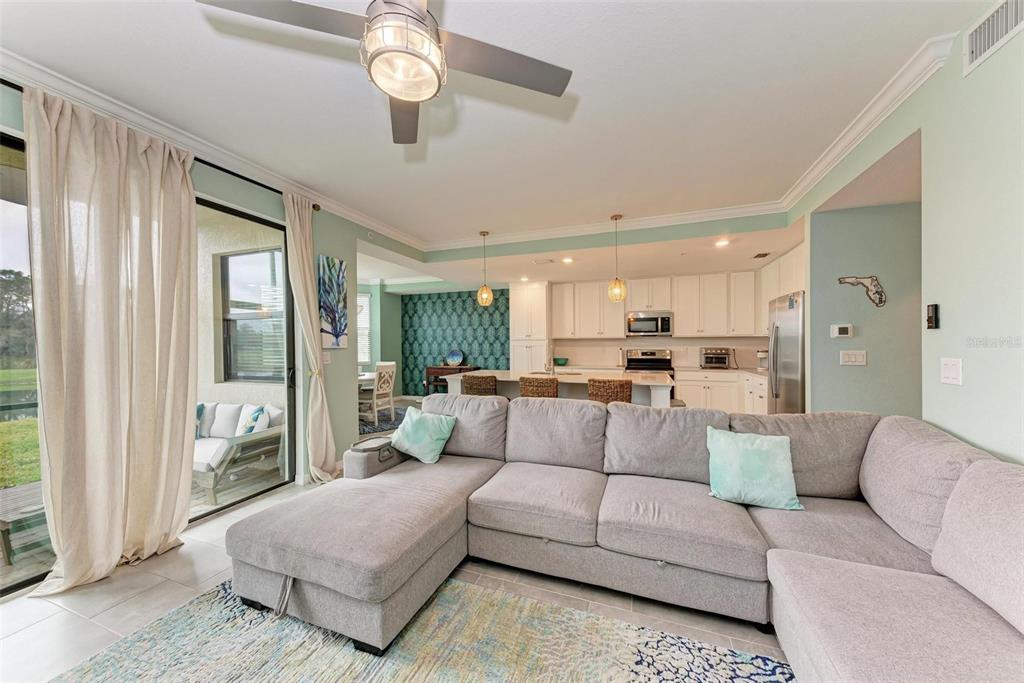 A living room with a gray sectional sofa opens to a kitchen with white cabinets — 18114 GAWTHROP DRIVE UNIT 103, BRADENTON, FL