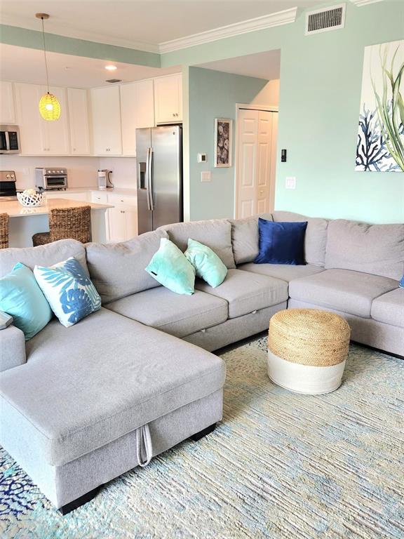 A light-filled living room features a large gray sectional sofa and an open-concept kitchen — 18114 GAWTHROP DRIVE UNIT 103, BRADENTON, FL