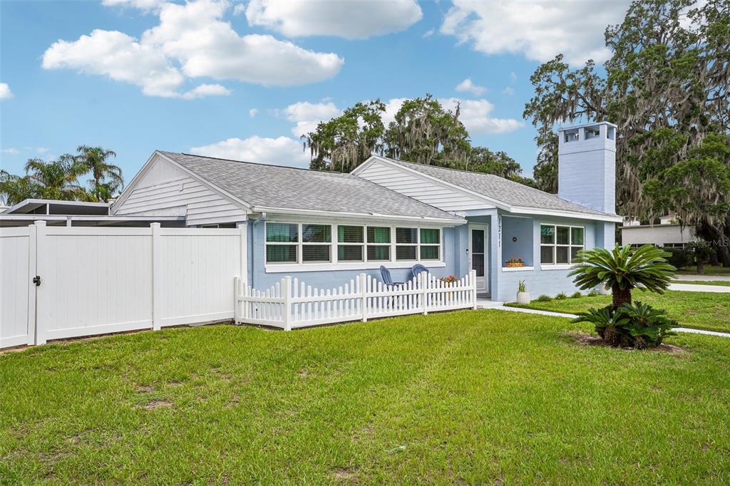 A light blue single-story house features a white picket fence, a walkway, and a porch — 1211 MORNINGSIDE DRIVE, MOUNT DORA, FL