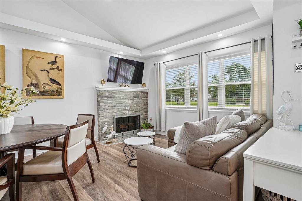 A living and dining area features a stone fireplace, wood-look flooring, and large windows — 1211 MORNINGSIDE DRIVE, MOUNT DORA, FL