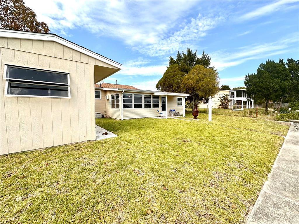 A beige house with a sunroom and a grassy backyard under a blue sky — 4016 EAGLE NEST DRIVE, HERNANDO BEACH, FL