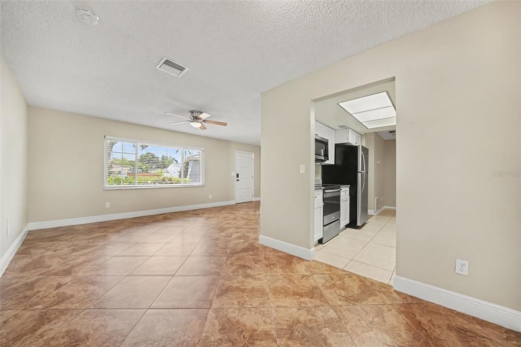 A living room with tan tile floors and a ceiling fan leads into a kitchen — 7925 SEGOVIA STREET, ORLANDO, FL